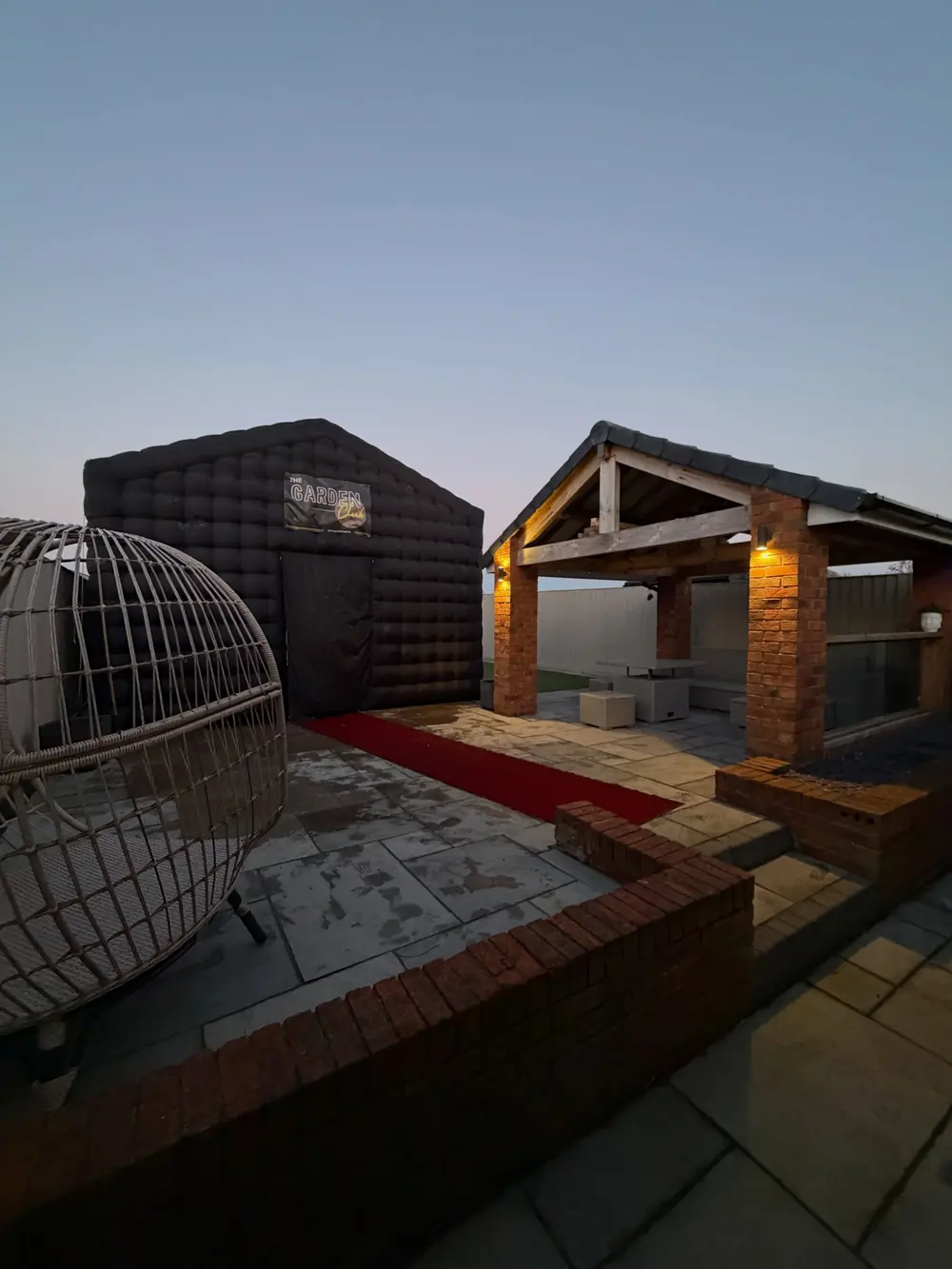 The club beside an oak pergola at dusk with a red carpet